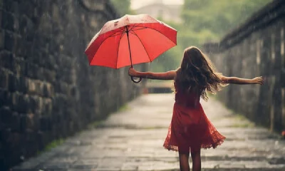 woman with red umbrella wearing red dress dancing in the rain