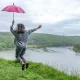 back view of a girl under an umbrella jumping near a lake in a mountainous area in rainy weather