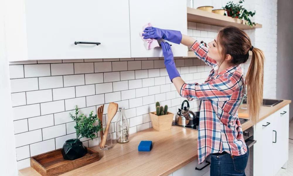 Woman in gloves cleaning cabinet with rag at home kitchen.