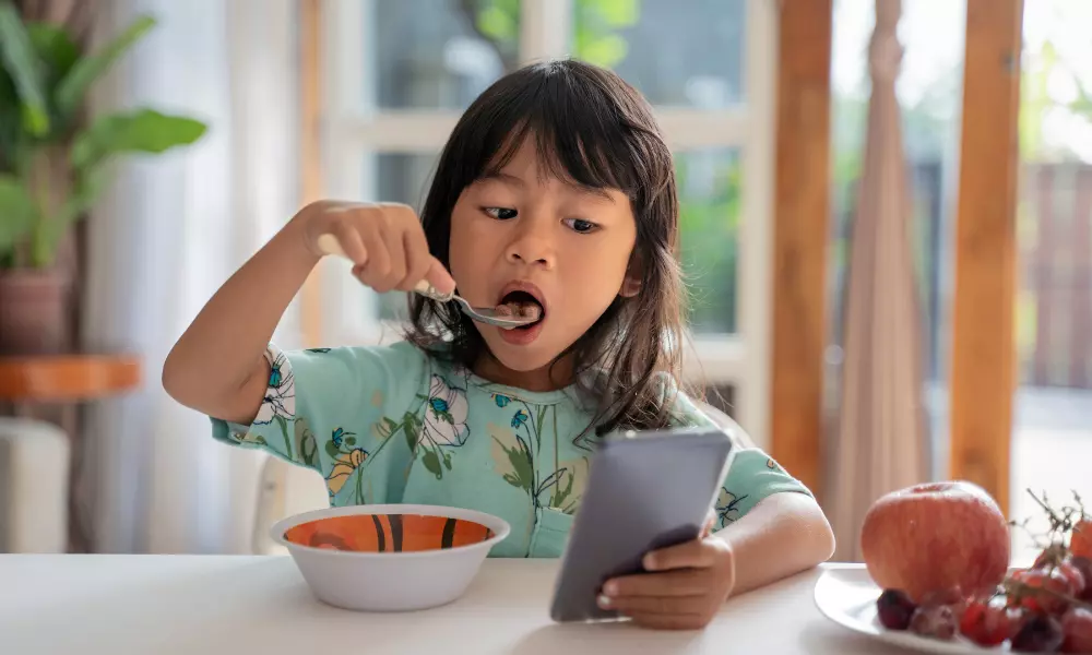 Distracted Kid Using Mobile Phone While Having Breakfast