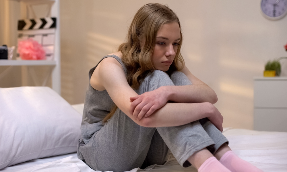 Pensive teen girl sitting alone in bedroom feeling abandoned, puberty depression