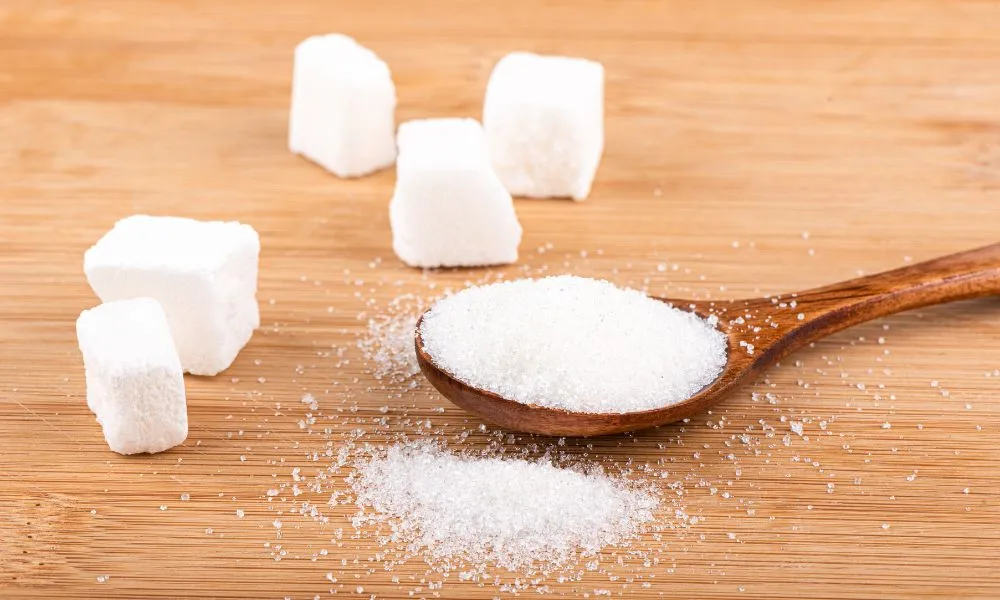 Lump sugar and a wooden spoon with white sugar on a wooden background.