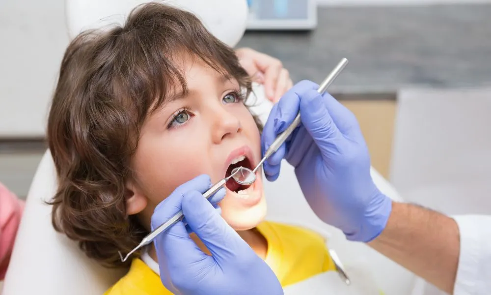 Pediatric dentist examining a little boys teeth in the dentists chair