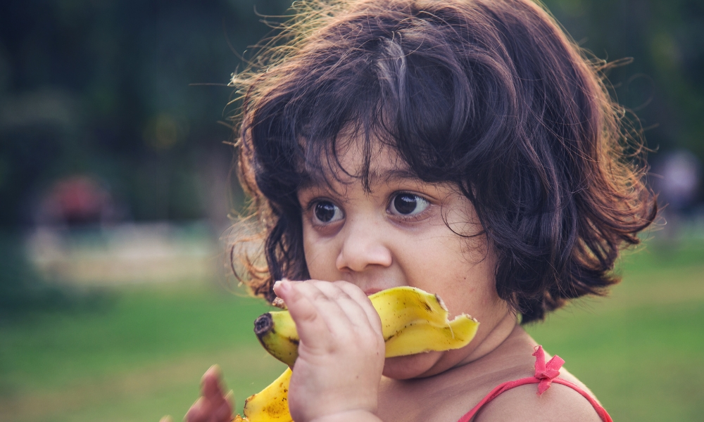 Indian kid eating banana outdoor.